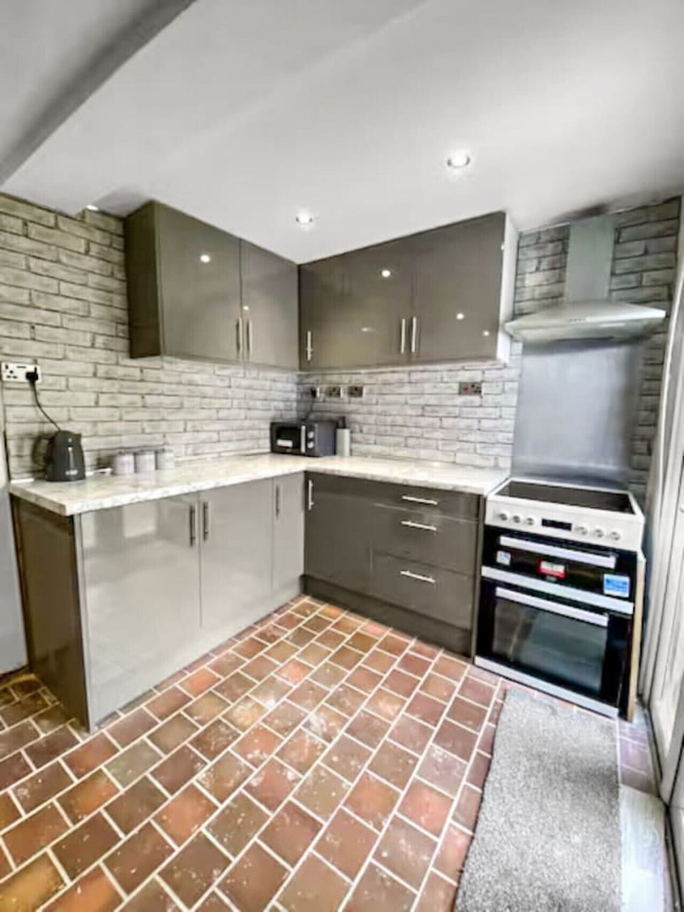 Grey gloss kitchen showing the hob, oven, refrigerator, microwave, and appliances set out on the worktop.