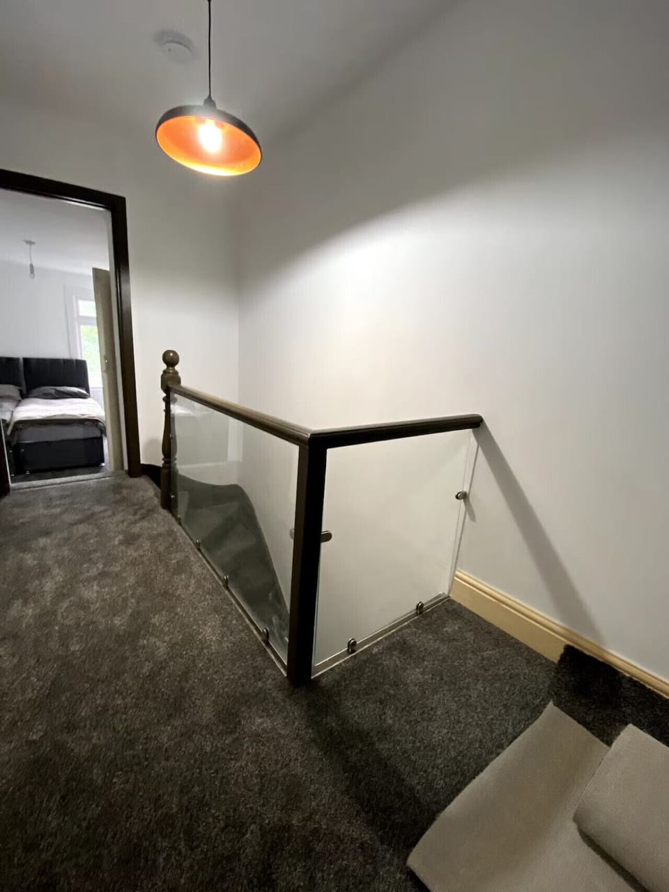 A staircase area with a glass-panelled metal bannister, carpeted treads, and a view along the upper landing.