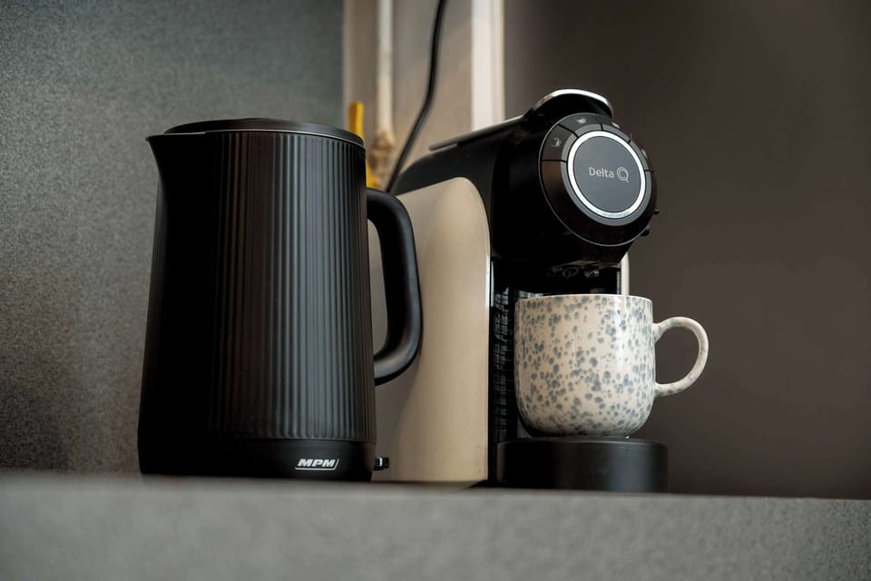 A functional kitchen corner features a black electric kettle and a modern coffee machine with a white mug. This setup provides a convenient coffee station for guests.