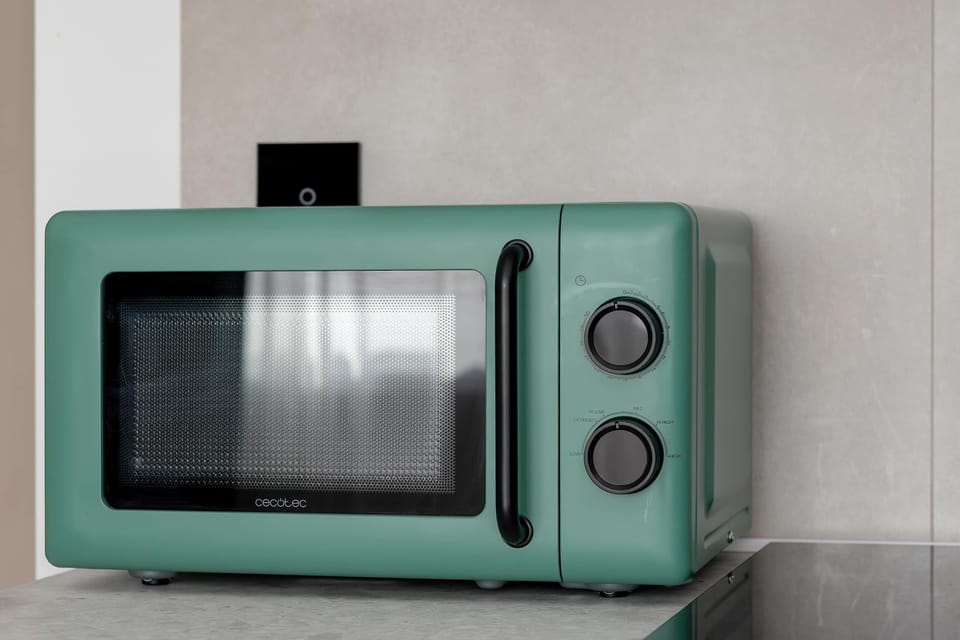 A retro-style microwave in a mint-green color placed against a neutral wall. Two round control dials are visible on the front. The appliance adds a vintage aesthetic to the kitchen setup.