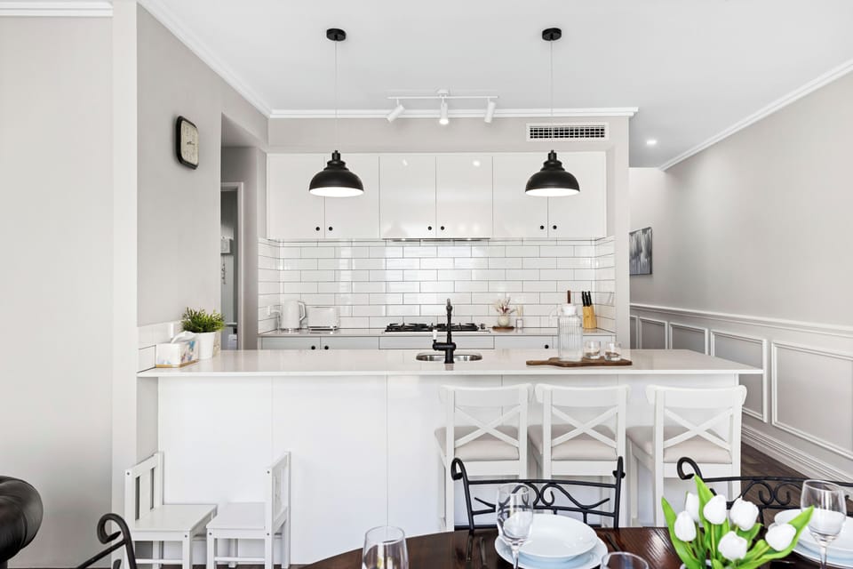 Cook up something special in this sleek, modern kitchen featuring crisp white subway tiles, industrial pendant lighting, and a spacious breakfast bar for casual morning coffee.