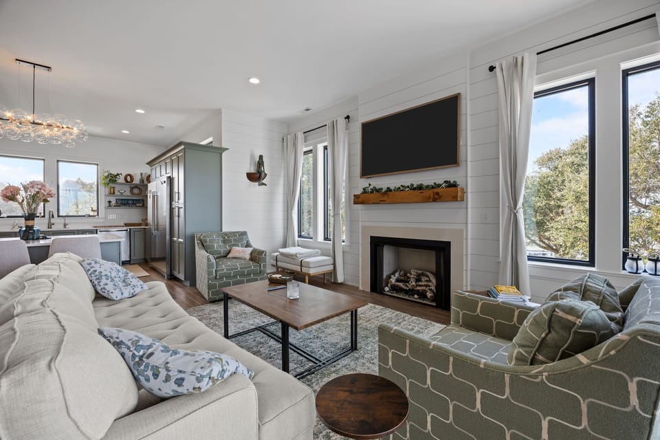 Gather by the fireplace in this bright living room, where modern comfort meets rustic charm with shiplap walls and treetop views.