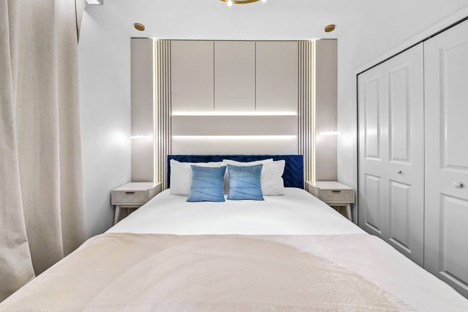Discover a cozy haven with a plush bed accented by soft blue pillows, inviting you to unwind. The sleek, modern headboard and warm lighting create a calming atmosphere, while stylish cabinetry offers practical storage solutions.