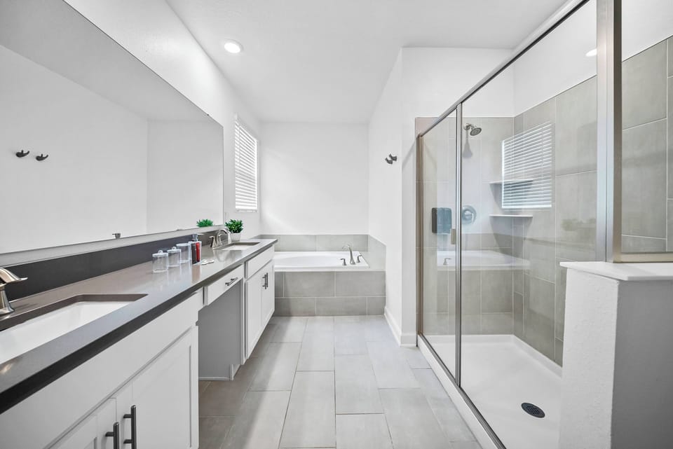 Step into this spacious bathroom featuring sleek gray tiles and a large glass shower that invites relaxation. The dual sinks with modern fixtures and a deep soaking tub create a functional yet stylish atmosphere for your stay.
