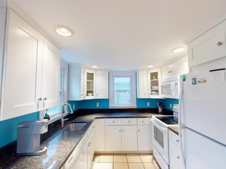 The kitchen is modern with white cabinetry, black countertops, and stainless steel appliances, accented by vibrant turquoise walls that add a fresh touch.