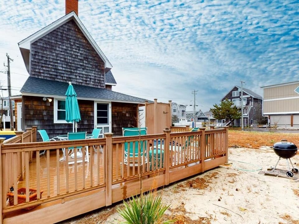 The outdoor deck offers a relaxing space with turquoise seating, perfect for enjoying the beachside atmosphere amidst nearby homes and vegetation.