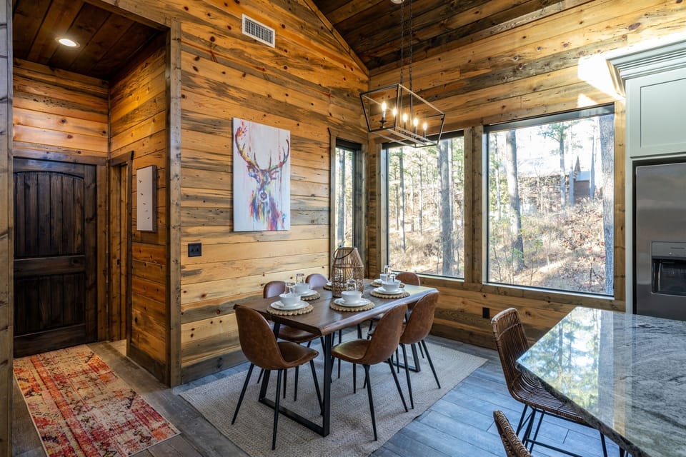 Enjoy meals in this dining area, featuring a modern wooden table, leather chairs, and views of the greenery through large windows.