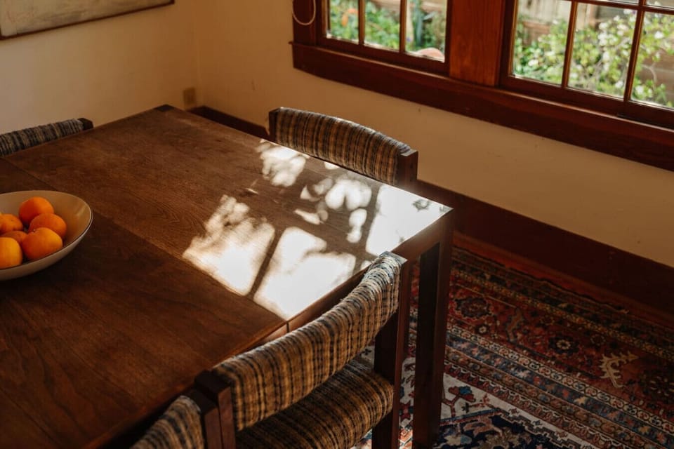 A beautifully styled dining table with rich wood grain, a bowl of fresh fruit, and soft natural shadows — simple, warm, and inviting.