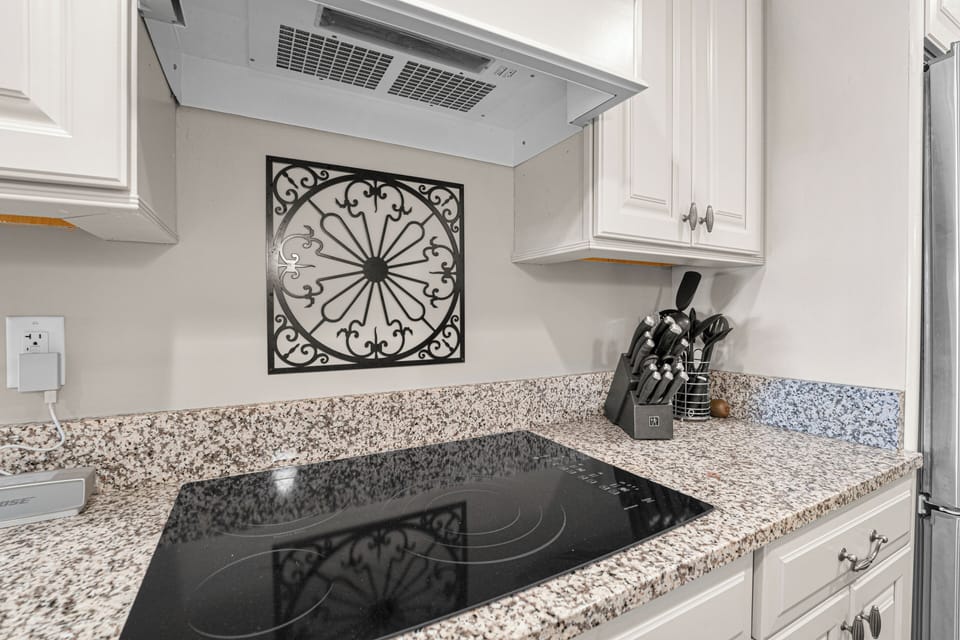 The kitchen features sleek granite countertops, a smooth glass cooktop, and well-appointed cabinetry stocked with essential cookware and utensils.