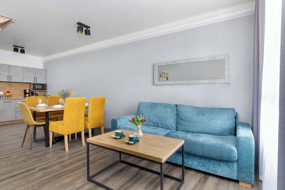 This wide shot shows the integration of the dining area and the living room with its teal sofa. The yellow dining chairs add a pop of bright color to the neutral grey walls.