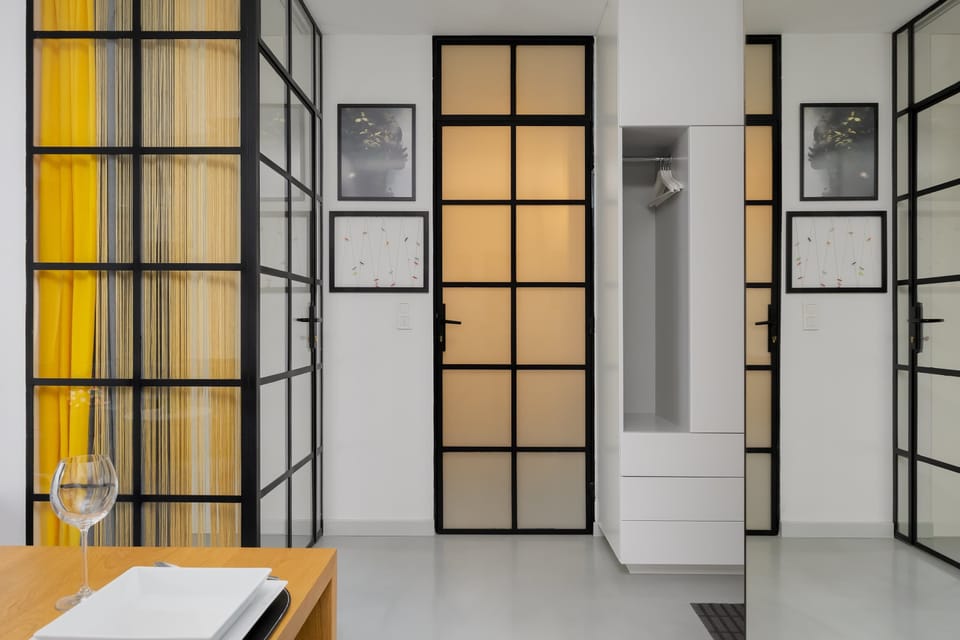 A hallway area with large yellow-framed glass doors. Framed pictures hang on the walls nearby. Clean white walls and modern lighting make the space feel bright and organized.