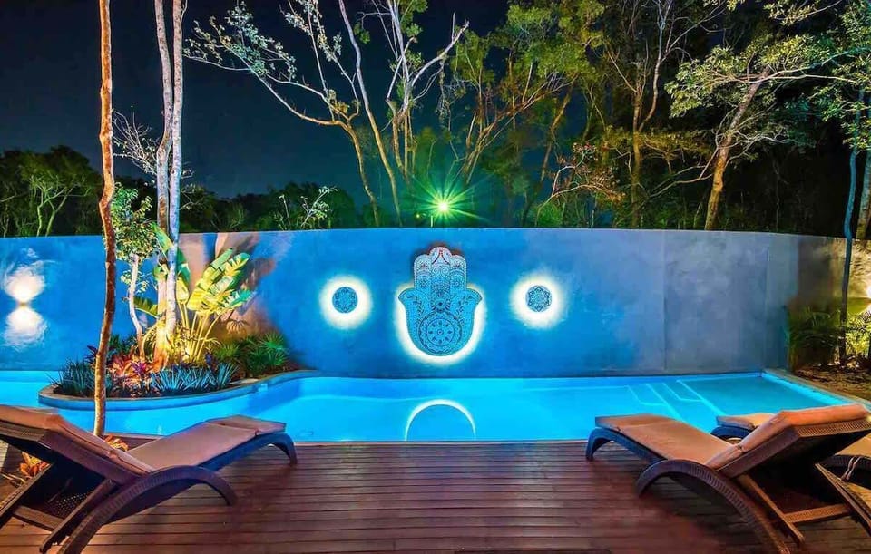 Dramatic nighttime pool view with designer Hamsa hand feature wall and lit pool steps.