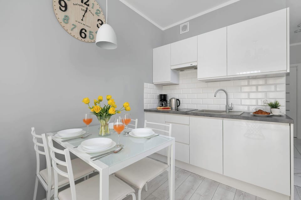 This angle captures the modern white kitchen with wood-look countertops. Next to the sink, a plate with breakfast food and fruits can be seen on the table.