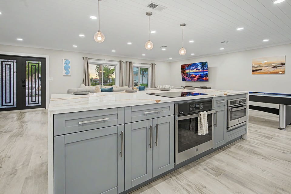 Your spacious open-concept kitchen flows seamlessly into the living area, featuring a large island with modern appliances, pendant lighting, and views of the outdoor oasis.