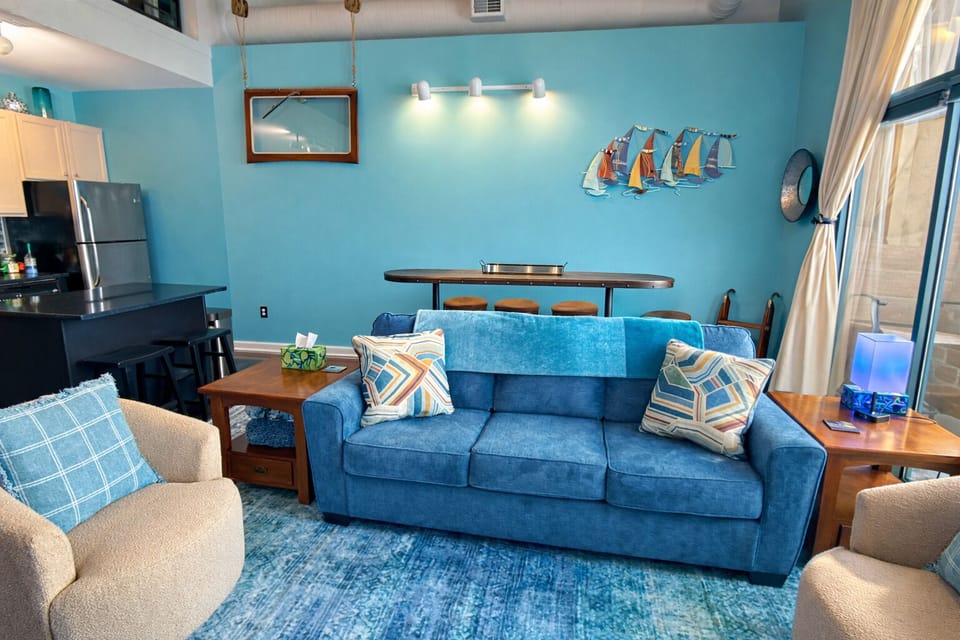 Stylish dining table behind plush seating offers a perfect spot for meals, games, or conversation. Soft coastal tones and natural light make this space feel welcoming and comfortable.