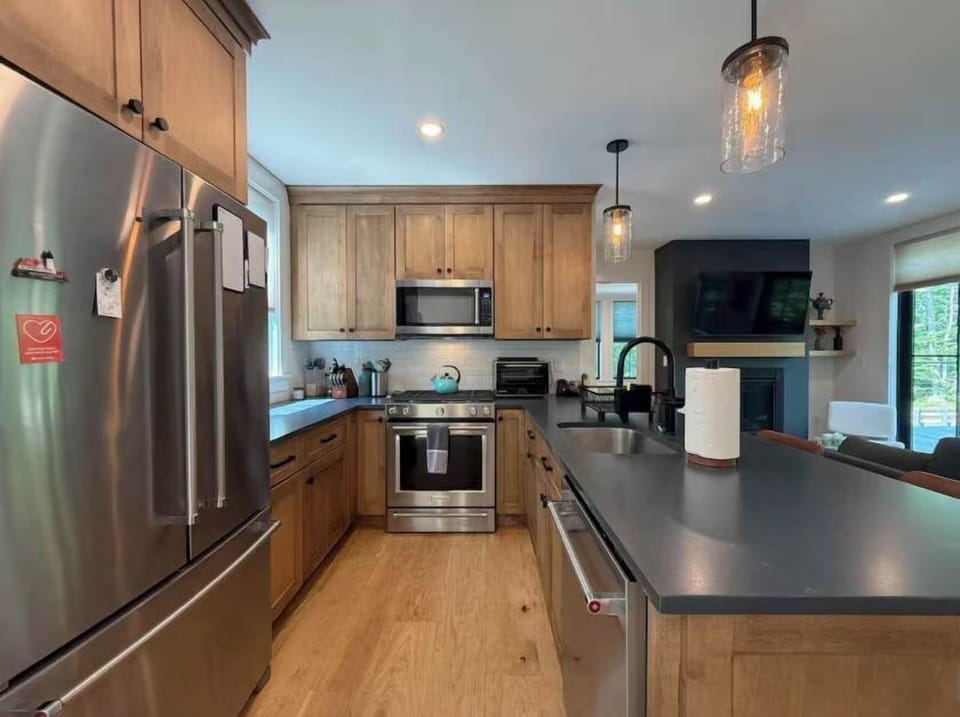 The kitchen is built for group cooking — warm wood cabinetry, stainless appliances, and a peninsula with seating for four at the center of it all.