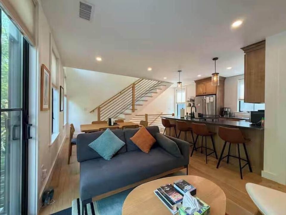 The open-riser staircase connects the floors in style — the kitchen peninsula and pendant lighting are visible just beyond the second-floor living area.