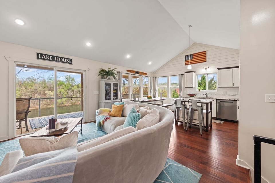 Bright open living room with plush sectional, floor-to-ceiling windows, and lake views