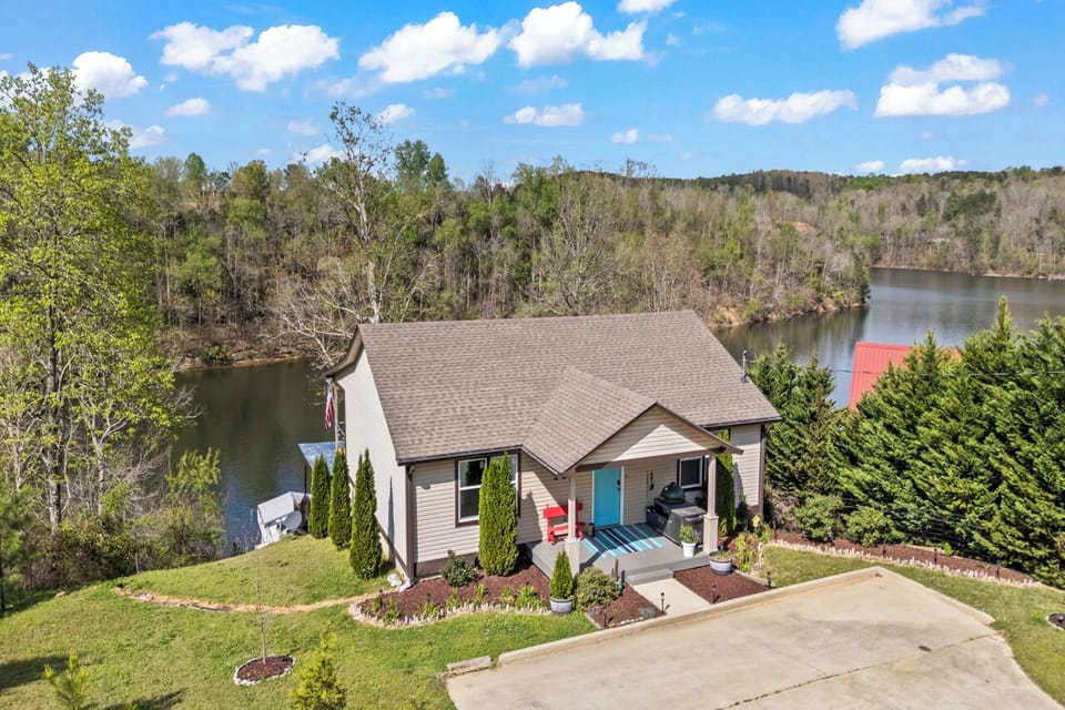 Aerial view of the home showing the stucco exterior, landscaped yard, and lake just beyond the trees