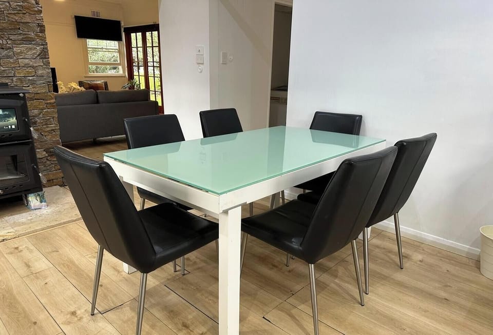 A modern and neat dining room featuring a sleek glass-topped table and contemporary black chairs.