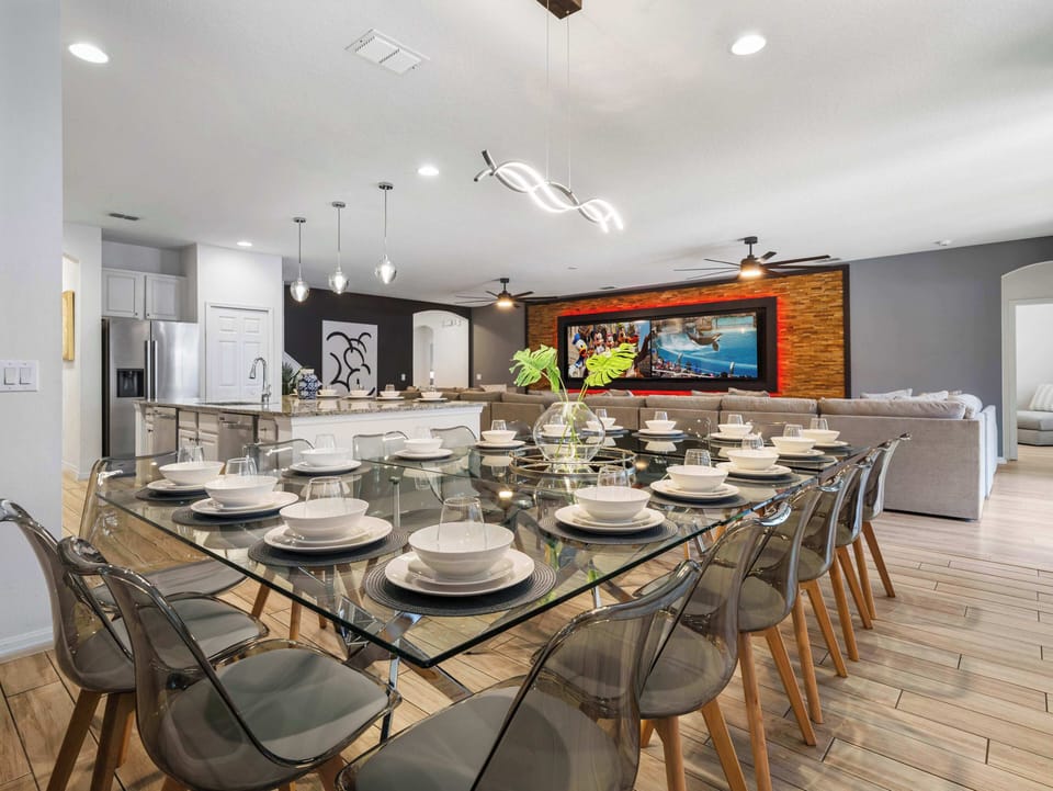 Sleek glass dining table set for a crowd beside an open kitchen & spacious lounge area