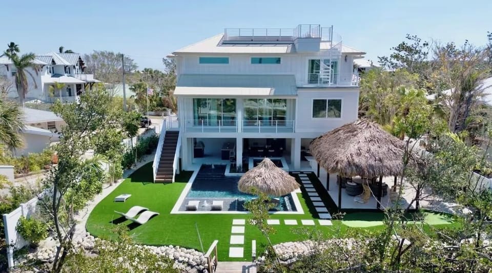 Modern waterfront villa featuring multiple levels, private pool, and tropical thatched pavilions set in lush landscaped grounds.