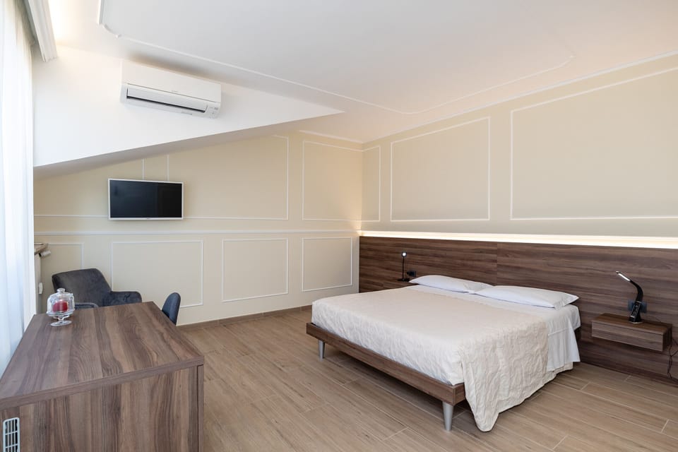 Modern and bright double bedroom in our Verona accommodation, furnished in a contemporary style with warm colors. The room features a double bed, air conditioning, flat-screen TV, desk, and soft lighting, ideal for a comfortable and relaxing stay.