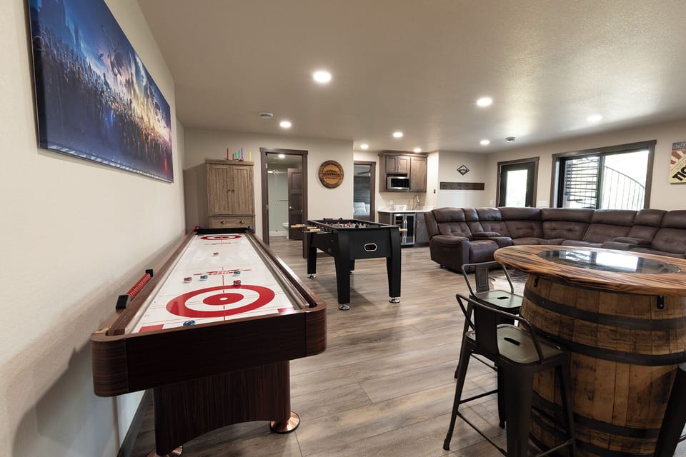 Spacious lower-level game room featuring shuffleboard, foosball, pub seating, and a cozy lounge area for movie nights and friendly competition.