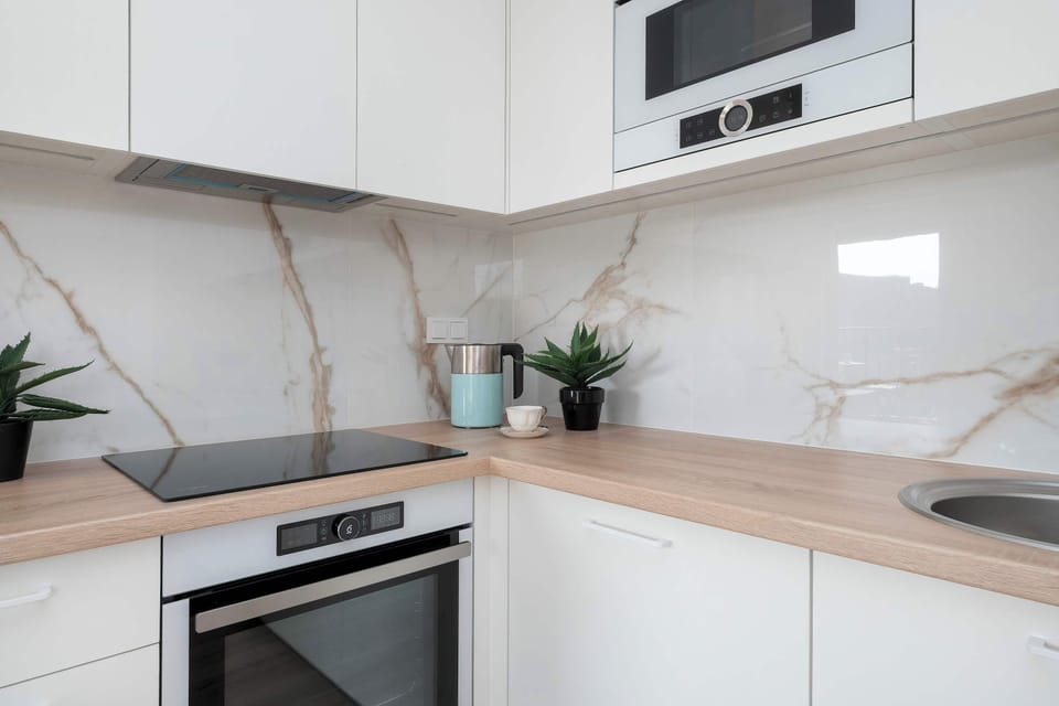 A kitchenette corner with a stovetop and countertop workspace. The white cabinets and light surfaces create a minimalist style.