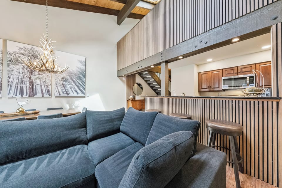 Sink into the plush sofa and take in the open-concept design, where soaring ceilings and rustic wood beams blend seamlessly with modern finishes and a welcoming kitchen ready for your mountain getaway.