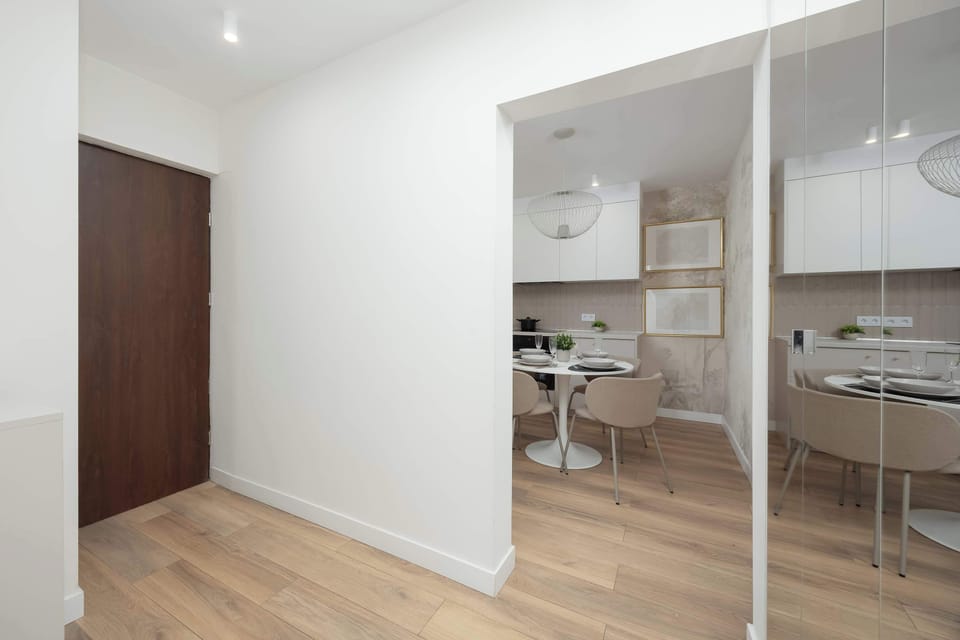 A view from the hallway looks back into the main living and dining area through a large mirror. The reflection highlights the bright and open nature of the apartment's floor plan.