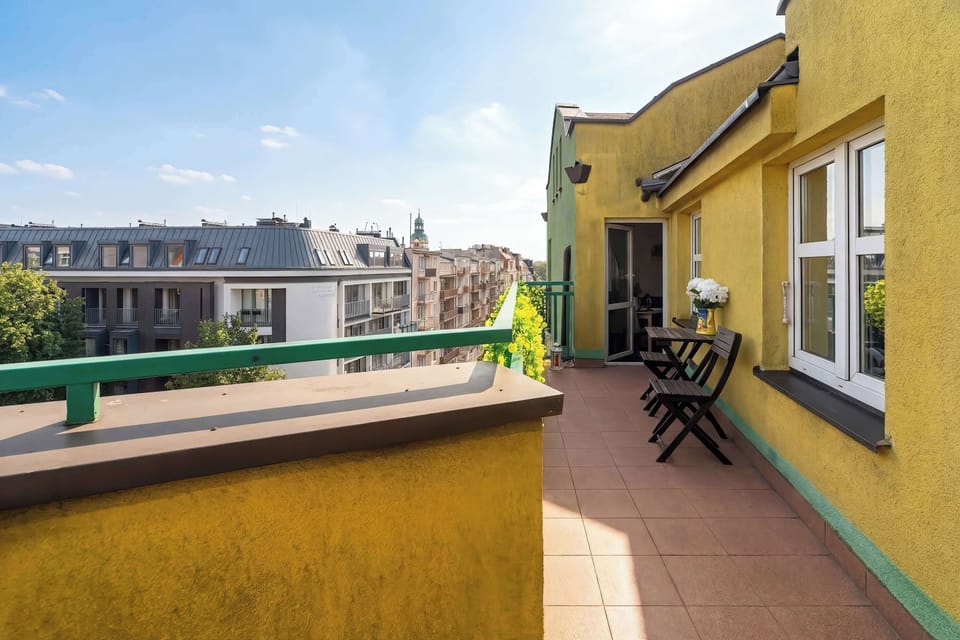A long balcony walkway with yellow exterior walls and railings, leading toward a view of the neighborhood.