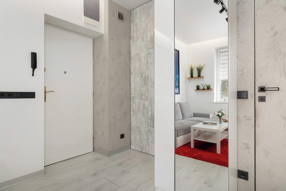 An entryway with the studio's entrance, featuring a large mirror and an intercom on a white wall. The simple layout makes it easy to find your way around the apartment.