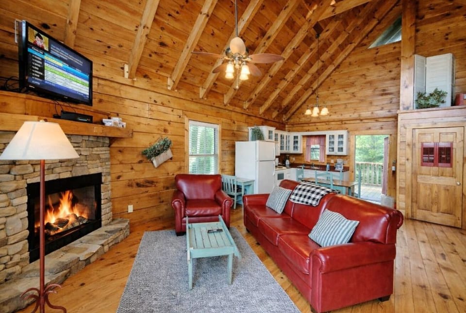 Inviting living room with a glowing stone fireplace, leather sofa, and flat-screen TV at Adorable Shut'er Inn in Pigeon Forge, Tennessee — a romantic couples retreat minutes from Dollywood.