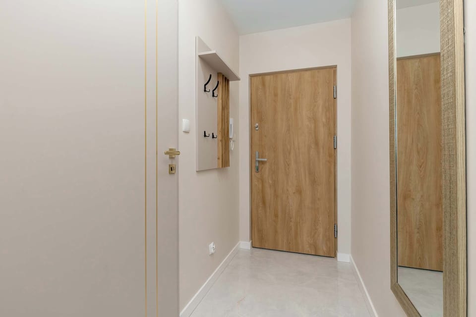 A hallway with light walls and wooden doors. The flooring is clean and polished, reflecting light. The space appears narrow but well-organized.