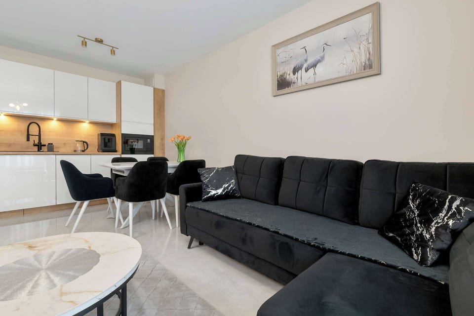 A spacious lounge area with a large L-shaped sofa and framed wall art above it. The lighting is soft and warm, enhancing the neutral palette. The layout emphasizes comfort and relaxation.