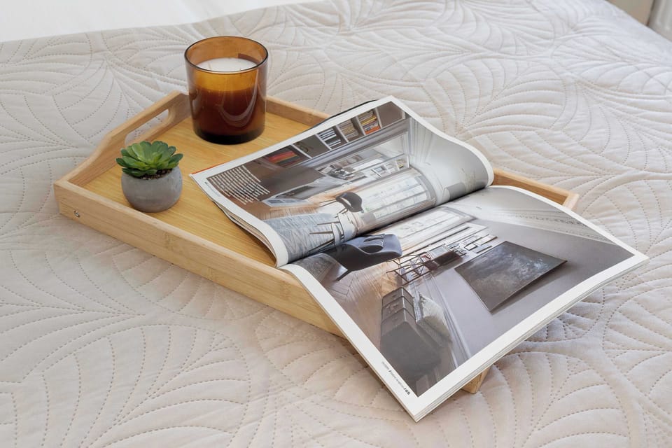 A tray on a bed with a book and small decorative items. The setup suggests relaxation and comfort. Soft textures enhance the cozy feel.