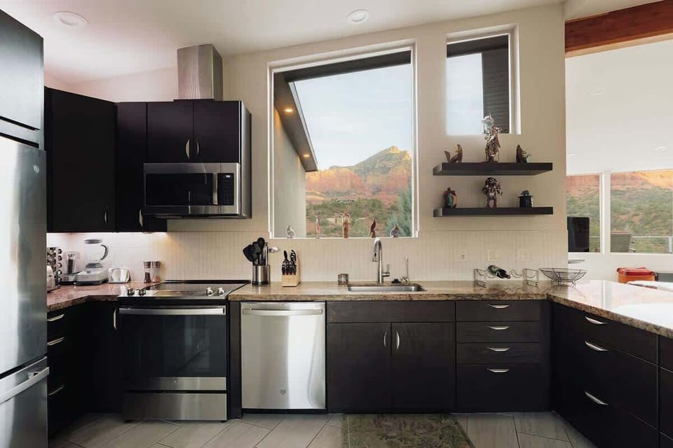 Your gourmet kitchen features sleek dark cabinets, granite counters, and stainless appliances, perfectly framed by dramatic mountain views through oversized windows.