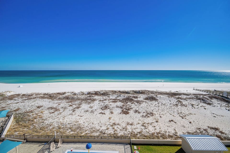 The shimmering shore stretches wide under a clear blue sky as you relax near the pool below