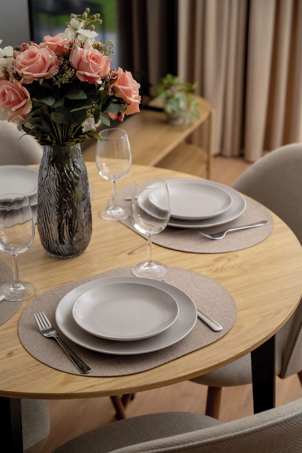 A dining table close-up shows a neatly set table with grey plates and clear glassware. The wooden tabletop adds warmth to the modern interior design.