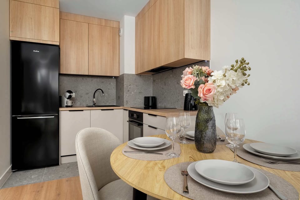 An L-shaped kitchen features a black refrigerator and modern wooden cabinetry. A dining table with a floral centerpiece sits in the middle of the room, perfect for entertaining.