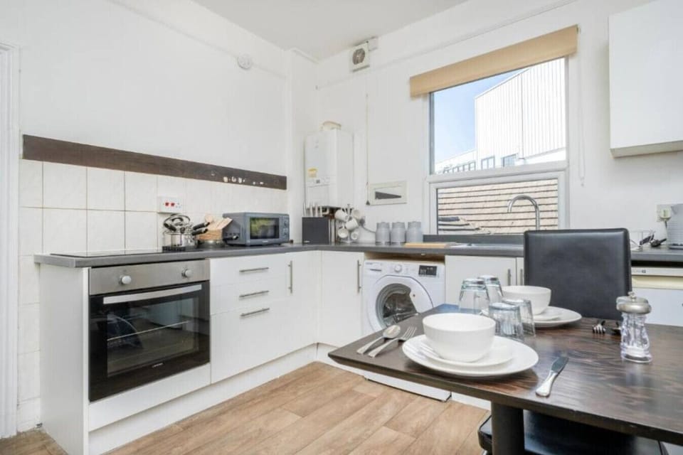White fitted kitchen with a built-in oven, hob, sink, and a dining table with chairs and place settings laid out.