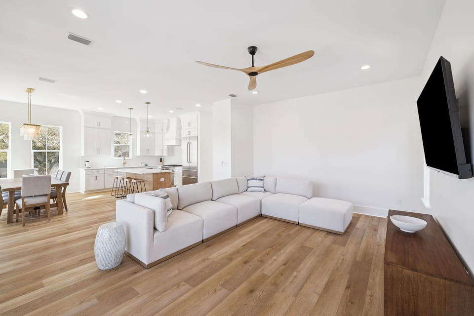 Relax in your spacious open-concept living area with plush sectional seating, warm hardwood floors, and modern kitchen nearby.