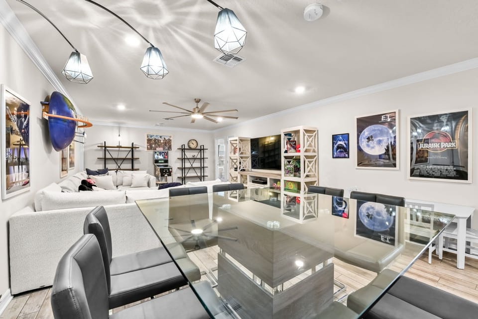 Spacious movie-themed living room designed for large groups with a large flat-screen TV, arcade games, pinball machine, and a dedicated table for games and gatherings.