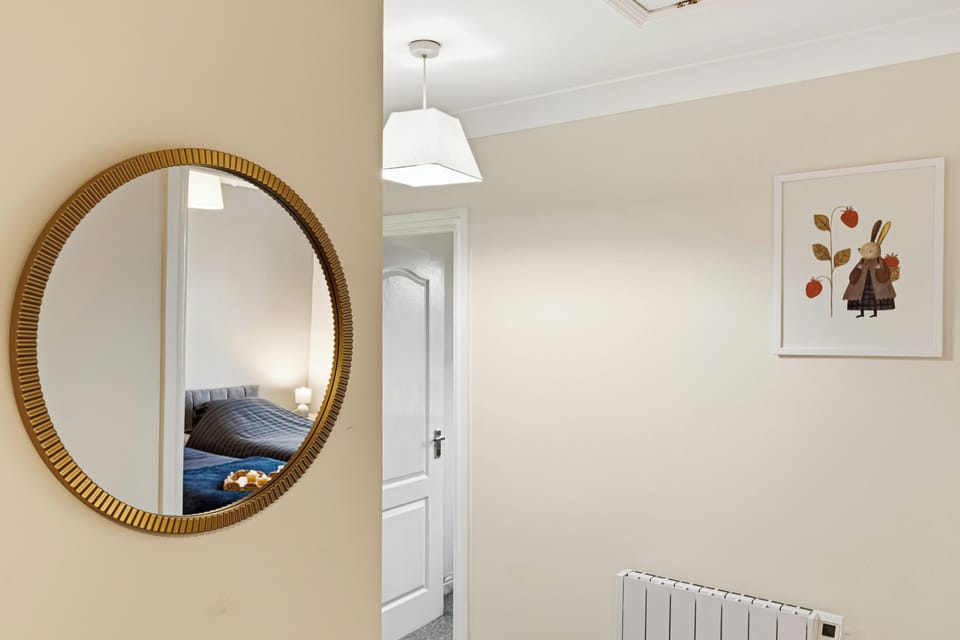 Bright, stylish hallway with mirror, artwork, and cozy bedroom glimpse