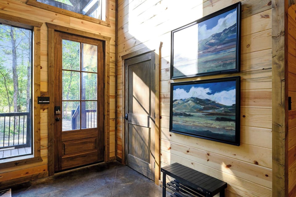 Framed mountain prints and a wood bench welcome you at the glass-front entry, the great room just beyond. - Entryway - The Hickorybear - Broken Bow, OK