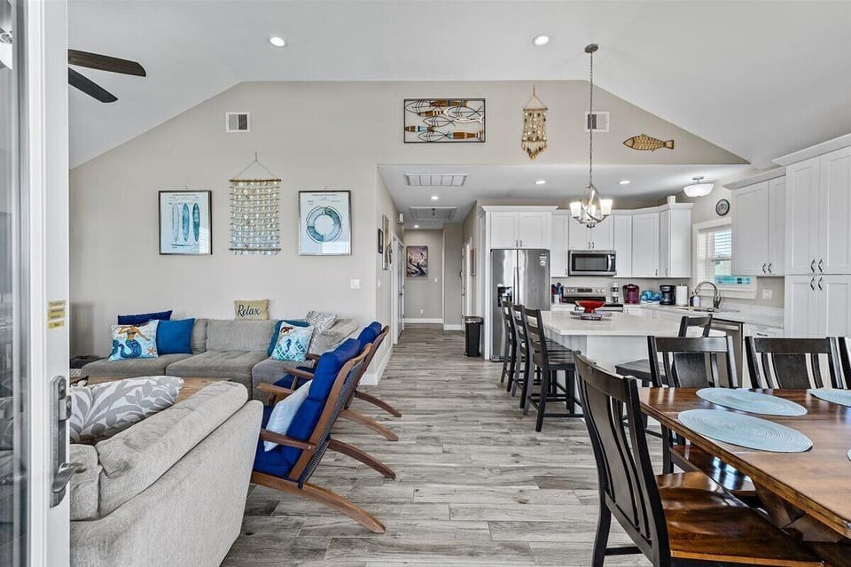 Large open-concept living and dining space with vaulted ceilings, modern coastal furnishings, and seating for large groups.