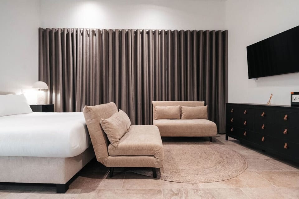 Unwind in this serene, modern bedroom featuring a plush king bed, cozy lounge seating, and a sleek wall-mounted TV—perfect for slow mornings or relaxing nights in.