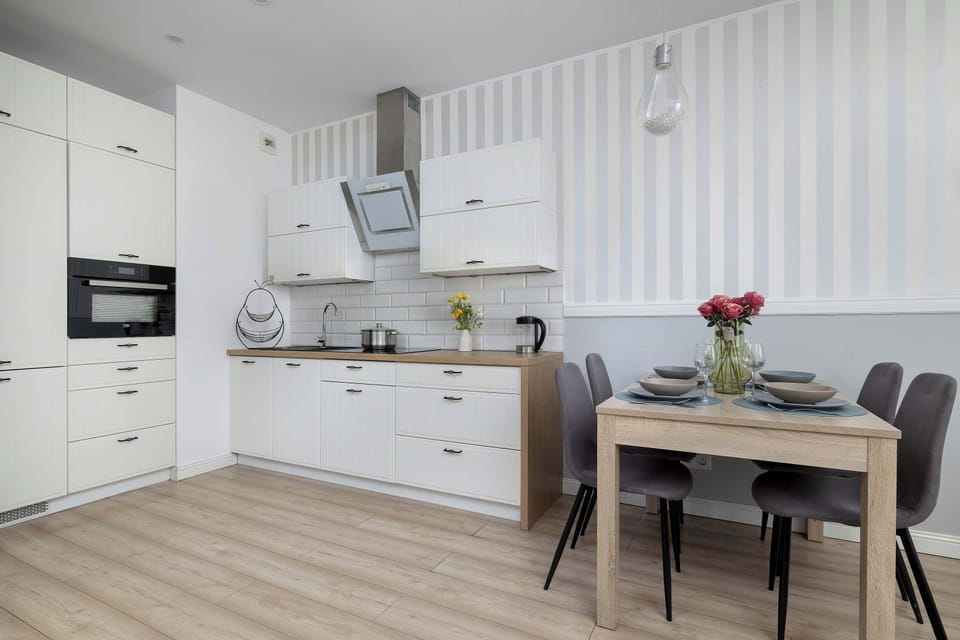 A dining table set for four people sits right next to the functional kitchen preparation area. The striped wallpaper design ties the dining and cooking zones together seamlessly.