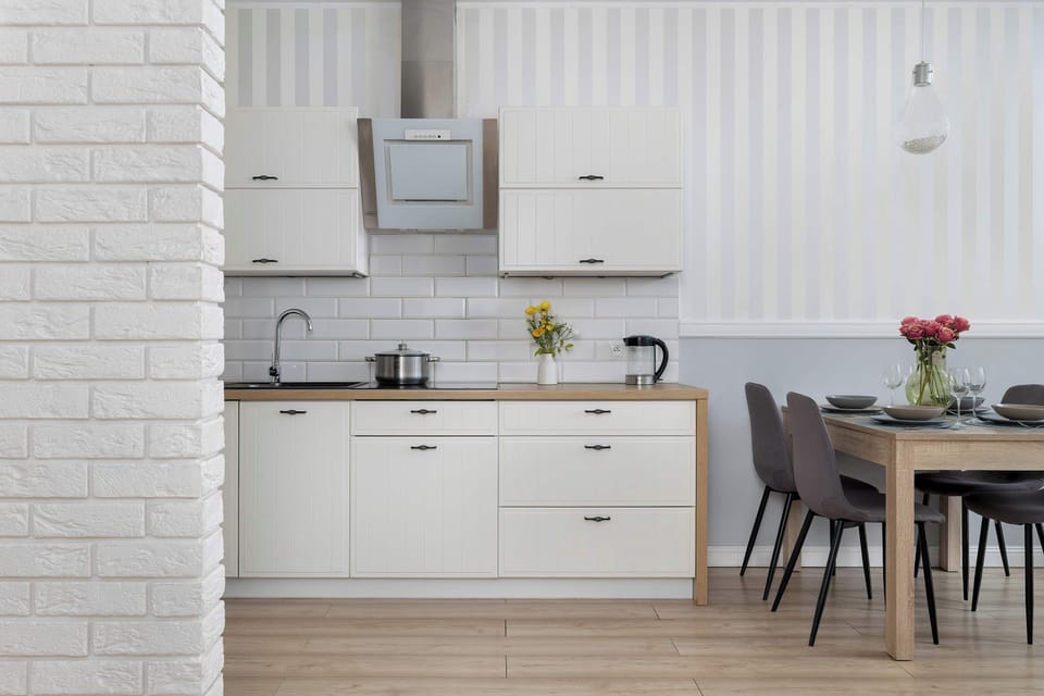 The white kitchen units are shown head-on to highlight the stainless steel extractor fan and clean lines. The wooden countertop is clear of clutter, emphasizing a minimalist and organized kitchen.